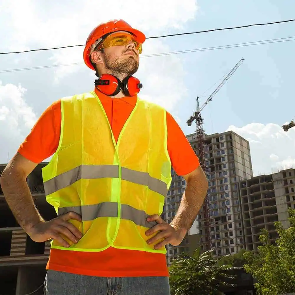 Construction worker in safety vest and helmet at a building site with cranes.