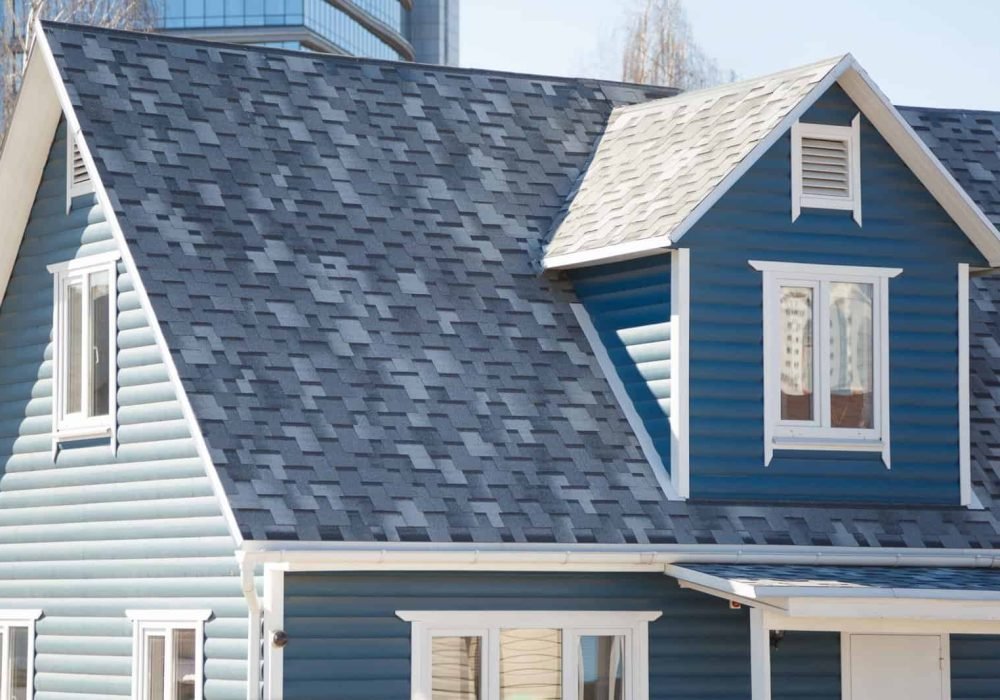 Blue house with gable roof and dormer window, showcasing roofing and siding services.