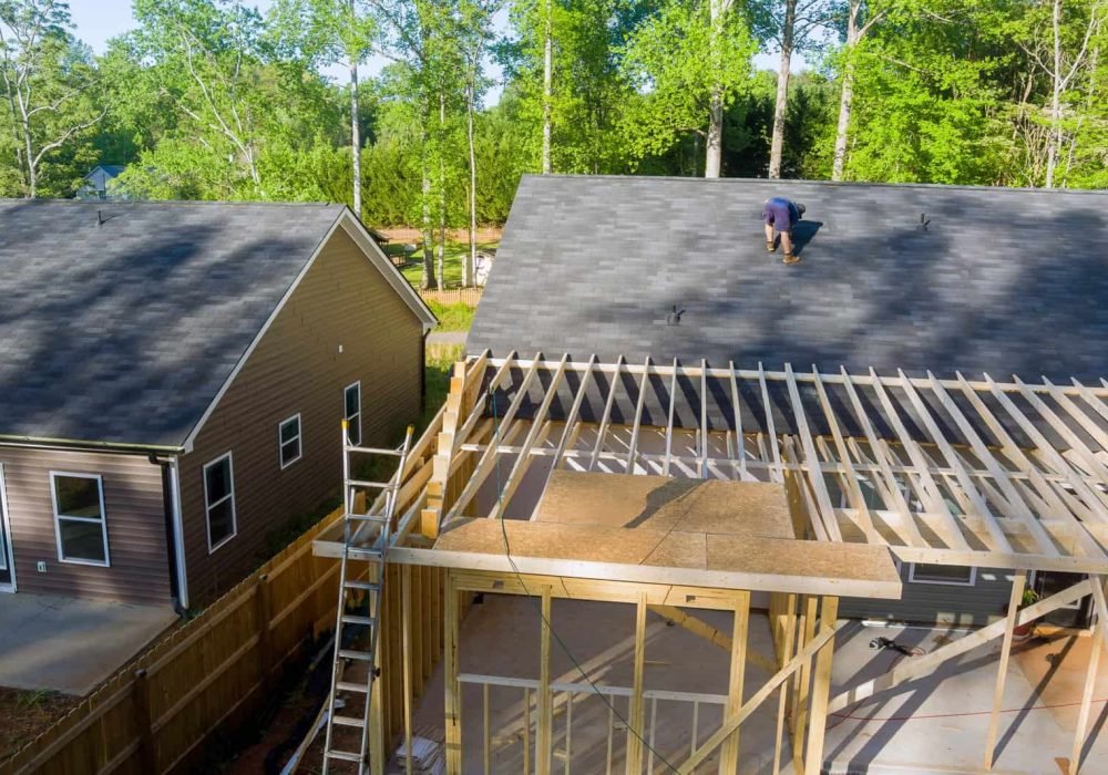 Roofing construction with worker installing shingles on a residential house.