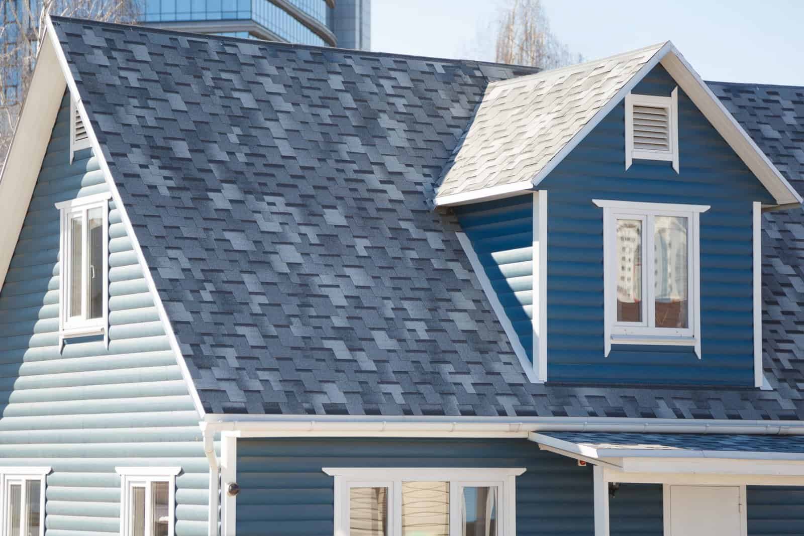 Blue house with gable roof and dormer window, showcasing roofing and siding services.