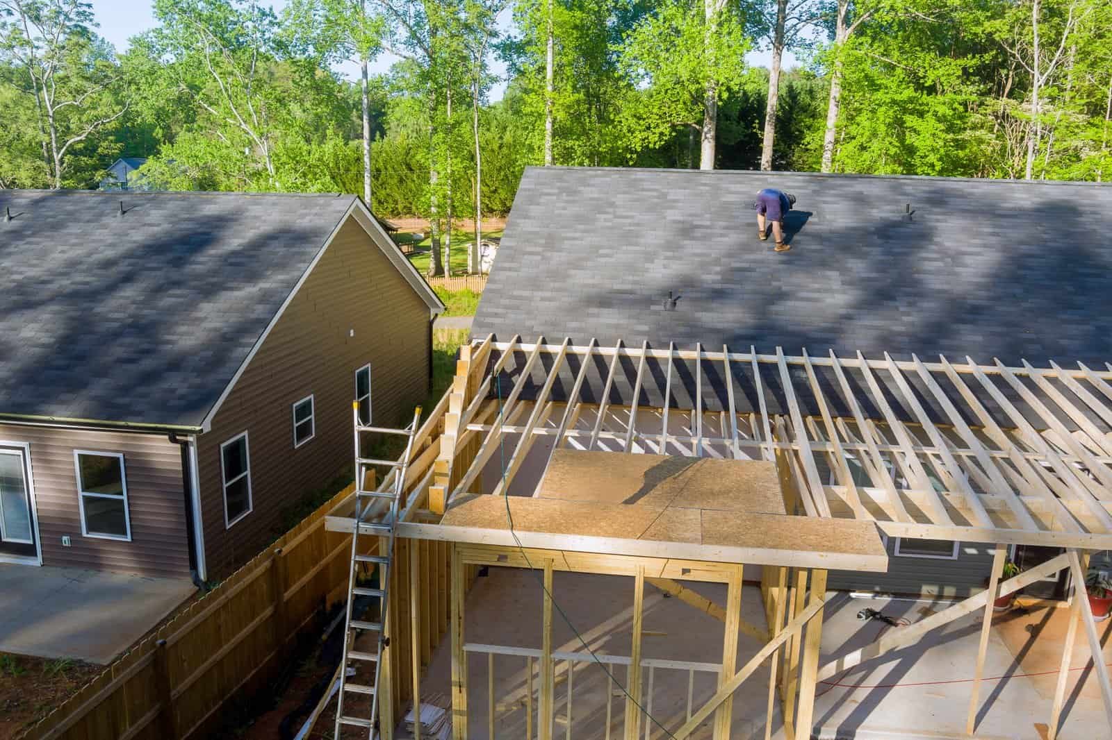 Roofing construction with worker installing shingles on a residential house.