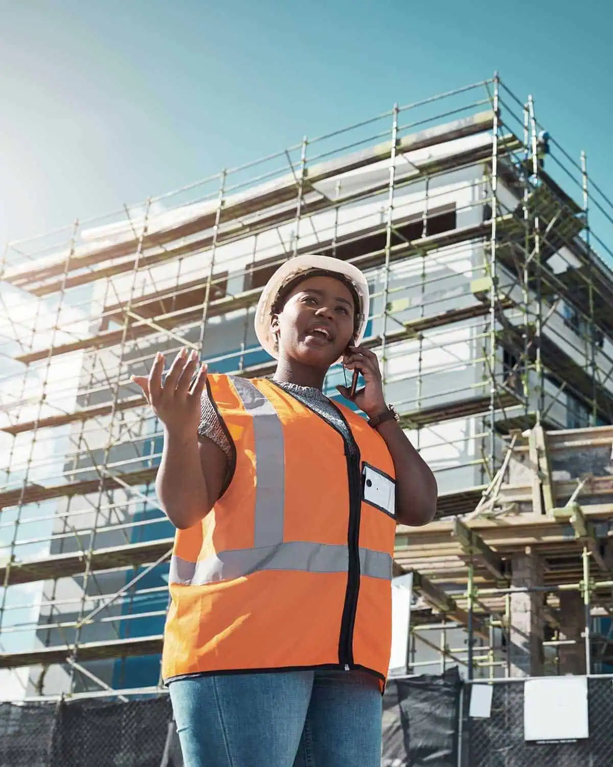 Construction worker in safety vest talking on phone at building site.